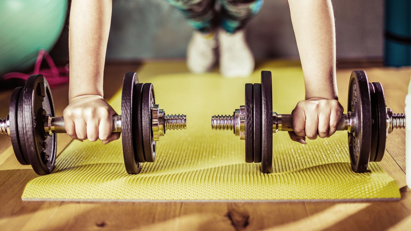 Hands gripping dumbbells on a workout mat